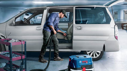 Man using a vacuum cleaner to clean the interior of a van in a garage setting.