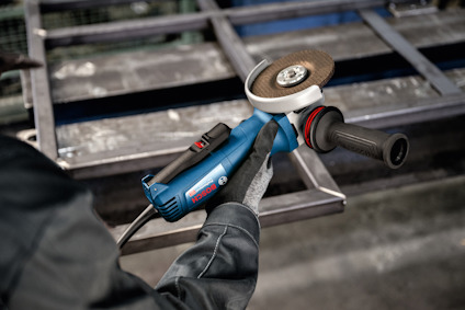 Vinkelslip med blått handtag används av person i arbetshandske, i bakgrunden en metallkonstruktion.