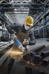 Arbetare i skyddsutrustning slipar metallbalk i industriell verkstad, gnistor yr runt.
