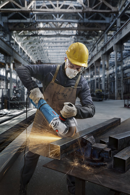Arbetare i skyddsutrustning slipar metallbalk i industriell verkstad, gnistor yr runt.