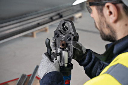 Person i arbetskläder använder en elektrisk presstång för att bearbeta ett metallrör.