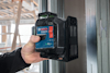 En person håller en Bosch Professional lasermätare framför en stålregel i en byggnad under konstruktion.
