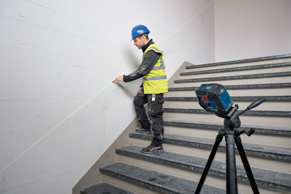 En person i säkerhetskläder arbetar med en laseravståndsmätare monterad på ett stativ på en trappa.