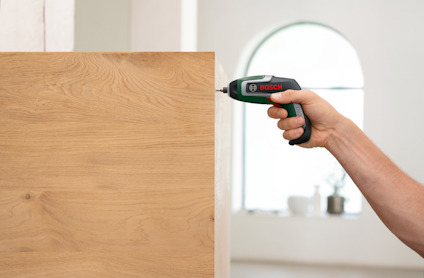 En hand använder en Bosch elskruvdragare för att skruva in en skruv i trä.