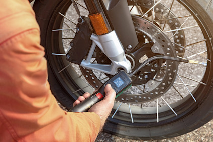 Person i orange jacka använder digital momentnyckel på motorcykelhjul.