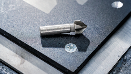 Metallkon eller borrhuvud placerad på en svart skiva av glas eller sten, med fästelement bredvid.