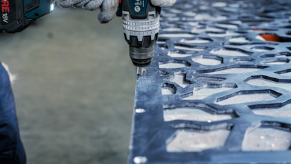 Hål borras i en perforerad metallplåt med en elektrisk borrmaskin.