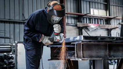 Person i skyddsutrustning slipar metall i en industrimiljö, gnistor flyger.