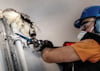 En person installerar rör i en vägg; skumplast och verktyg är synliga. Personen bär hjälm och ansiktsskydd.