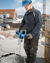 En person i hjälm använder en blå borrmaskin för att blanda cement på en byggarbetsplats.