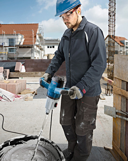 En person i hjälm använder en blå borrmaskin för att blanda cement på en byggarbetsplats.
