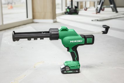 Grön och svart batteridriven fogpistol av märket HiKOKI ligger på ett golv i ett ljust rum med fönster.