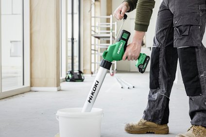 Person med mörka byxor och gröna handskar använder en grön Hikoki betongblandare i en vit hink.