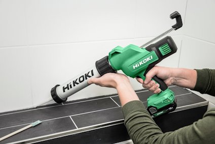 Händer som håller en grön HiKOKI batteridriven fogpistol som applicerar fogmassa vid kakelplattor.