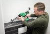 Person använder en grön Hikoki batteridriven fogspruta för att applicera fogmassa på kakel.