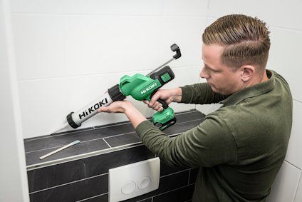 Person använder en grön Hikoki batteridriven fogspruta för att applicera fogmassa på kakel.