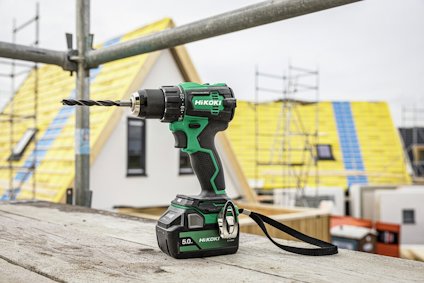 Sladdlös borrmaskin med gröna detaljer placerad på en byggnadsställning. Bostadshus under konstruktion i bakgrunden.