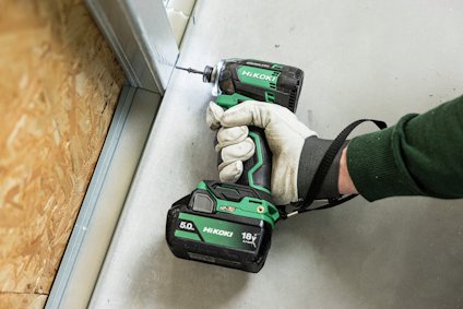Person håller en grön batteridriven skruvdragare med märket Hikoki, med en handske på, mot en metallprofil.