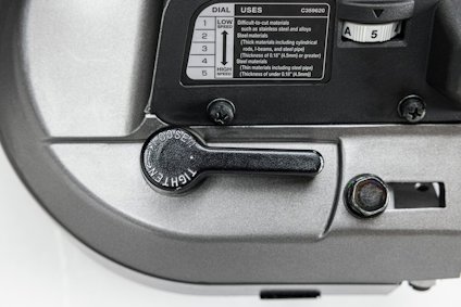 Närbild av en maskindel med en svart spak märkt "TIGHTEN" och en vridbar ratt med inställningar låg till hög.
