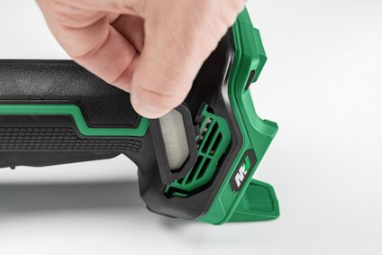 En hand håller i ett grönt och svart verktygshandtag med en vit knapp på sidan.