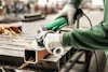 En person använder en grön HiKOKI vinkelslip för att kapa en metallprofil. Gnistor flyger från skärningen.