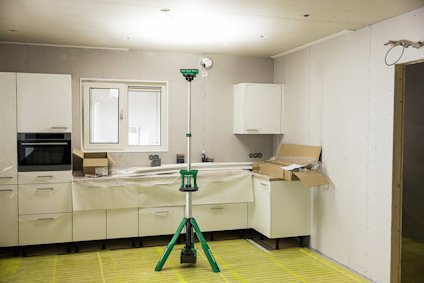 Kök under renovering med vit köksinredning. Ett grönt byggstativ står mitt i rummet.