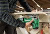 En person använder en grön Hitachi-verktyg för att kapa trä vid en arbetsbänk i en verkstad.