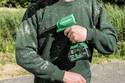 Person som håller en grön Hikoki-enhet mot en grön tröja täckt av träspån.