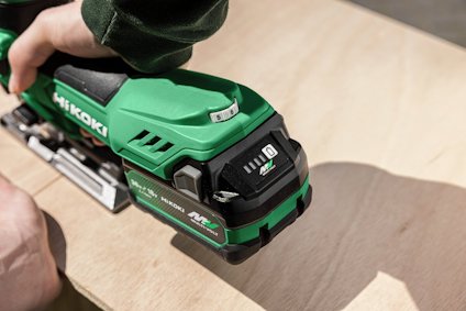 Grön och svart elektrisk sticksåg används för att skära plywood. Text på sågen: "HIKOKI MULTI VOLT". Hand synlig på sågen.