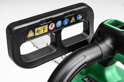 Svart handtag med säkerhets- och varningssymboler på en grön elektrisk anordning.