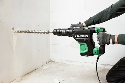 En person använder en HiKOKI slagborrmaskin för att borra i en vit vägg.
