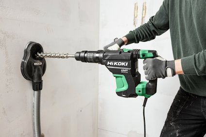 Person använder en HiKoki borrmaskin med dammsugartillbehör på en vägg.