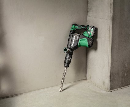 Grön och svart borrmaskin lutad mot ett grått betonghörn på ett grått golv.