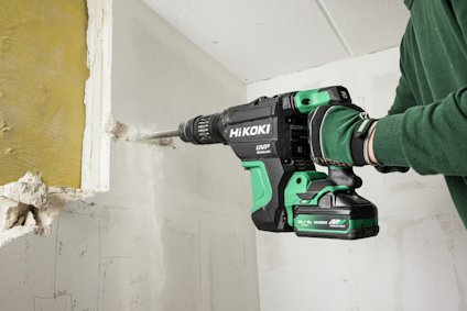 Hikoki borrmaskin används för att borra i en vägg av gips eller betong. Användaren bär gröna arbetshandskar.