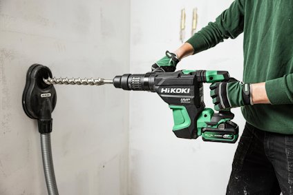 Person som använder en grön och svart Hikoki borrmaskin med en slanganslutning mot en vägg.