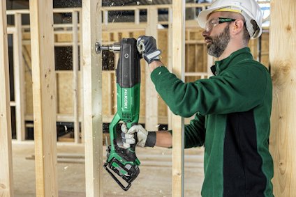 Man with safety gear using a green and black Hitachi power saw on wooden beams.
