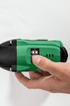 En hand trycker på knappen på en grön och svart elektrisk enhet, troligen en borrmaskin.