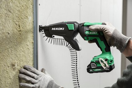 En person använder en grön och svart Hikoki skruvautomat för att fästa en skiva mot en vägg.