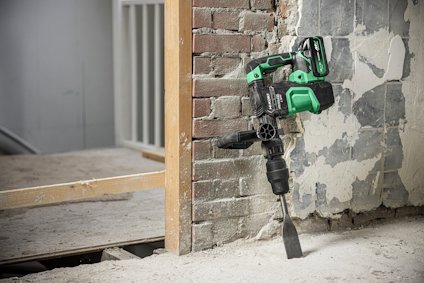 Grön och svart eldriven borrmaskin lutar mot en tegelvägg under renovering.