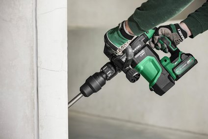 Person som använder en grön och svart borrhammare mot en vit vägg, iförd handskar.