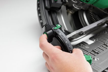 Hand justerar vinkel med grön och svart ratt på cirkelsåg med graderad skala.