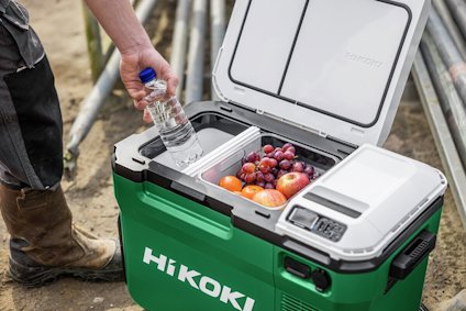 Grön kylbox med öppen lock visar flaskvatten och frukt inuti. Person i arbetskläder står intill boxen.