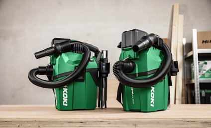 Två gröna Hitachi dammsugare placerade på ett träbord med tillbehör och slangar, med träplankor i bakgrunden.