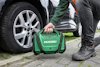 Person kneeling by car wheel, holding a green Hikoki tool case.