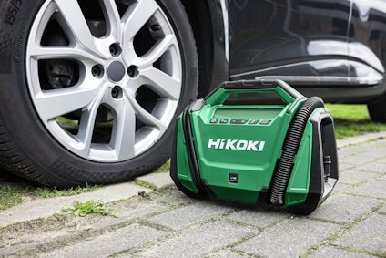 En grön HiKOKI-portabel kompressor bredvid ett bilhjul på gatsten.