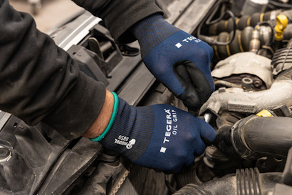 En person med mörka handskar arbetar med en motor. Text på handskarna: "TEGERA", "GRIP", "850".