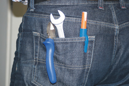 Verktyg i bakfickan på jeans, inklusive skiftnyckel, tång och penna med blått handtag.