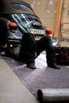 Person ligger under en svart klassisk bil i ett garage med verktyg bredvid. Registreringsskylt: PHK 373.