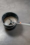 En hink med grå cementblandning och en vispstav nedsänkt i blandningen på grått golv.