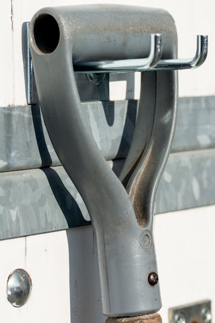 Grått plastskaft med två metallkrokar monterat på en dörr med galvaniserad panel.